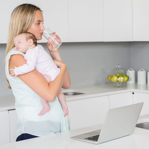 A woman holding a baby drinking water from the sink